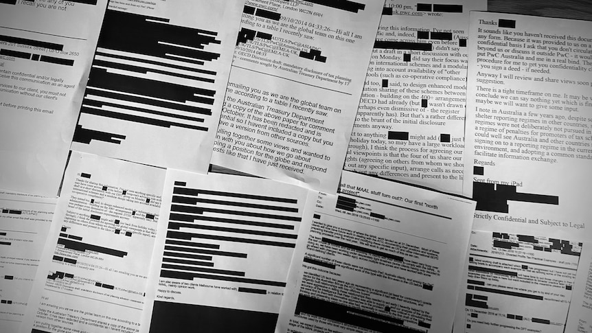 Printed black and white copies of emails laid out on a table with chunks of text redacted in black.