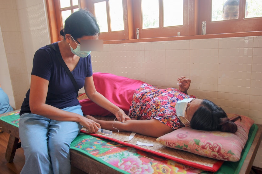 A woman holds a syringe with a tube attached to a woman's arm