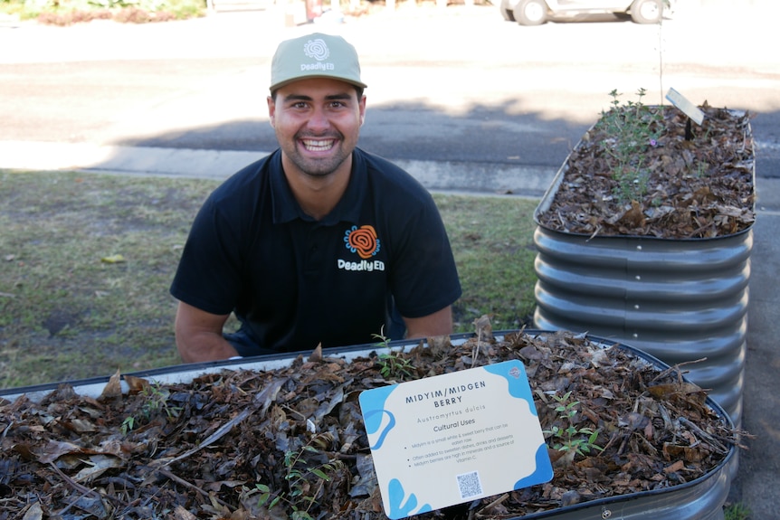 Deadly Ed worker smiles next to one of the native plants in the bush tucker garden 