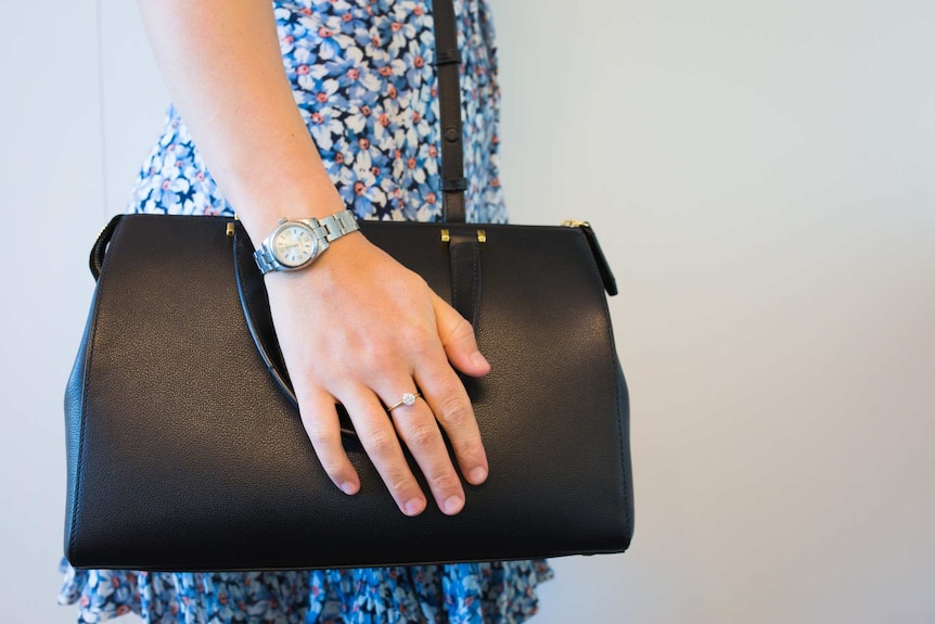 A woman holding a handbag with a diamond ring and watch.