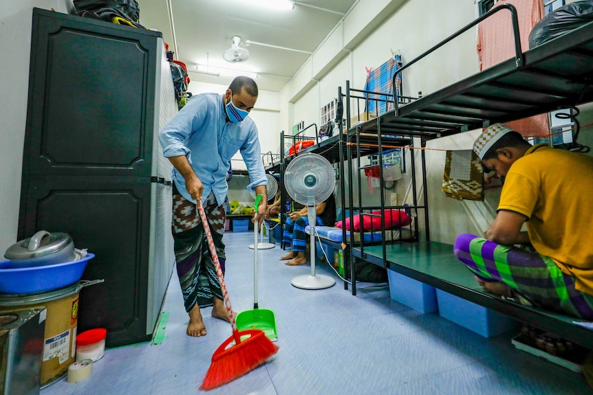 A man in a face mask sweeping a dorm room floor