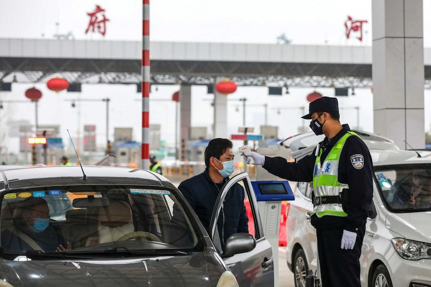 A policeman uses a digital thermometer to take a driver's temperature at a checkpoint at a highway toll gate in Wuhan.