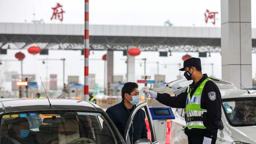 A policeman uses a digital thermometer to take a driver's temperature at a checkpoint at a highway toll gate in Wuhan.