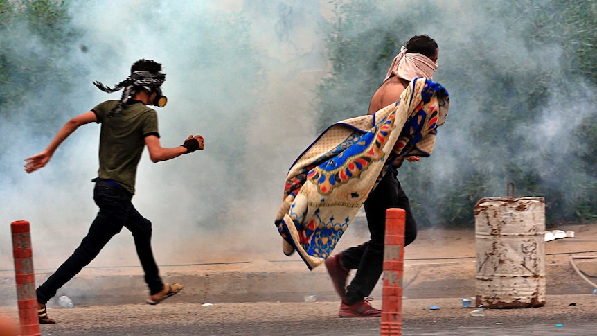 anti-government protesters walk through tear gas in Basra, Iraq