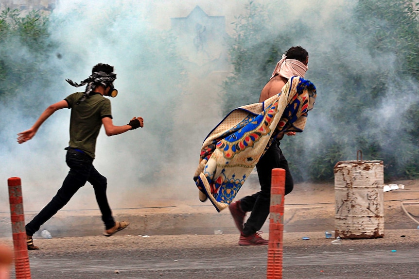 anti-government protesters walk through tear gas in Basra, Iraq