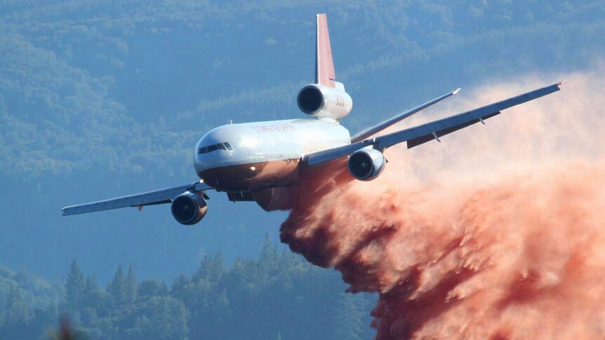 A very large air tanker drops red fire retardant on a forest fire.