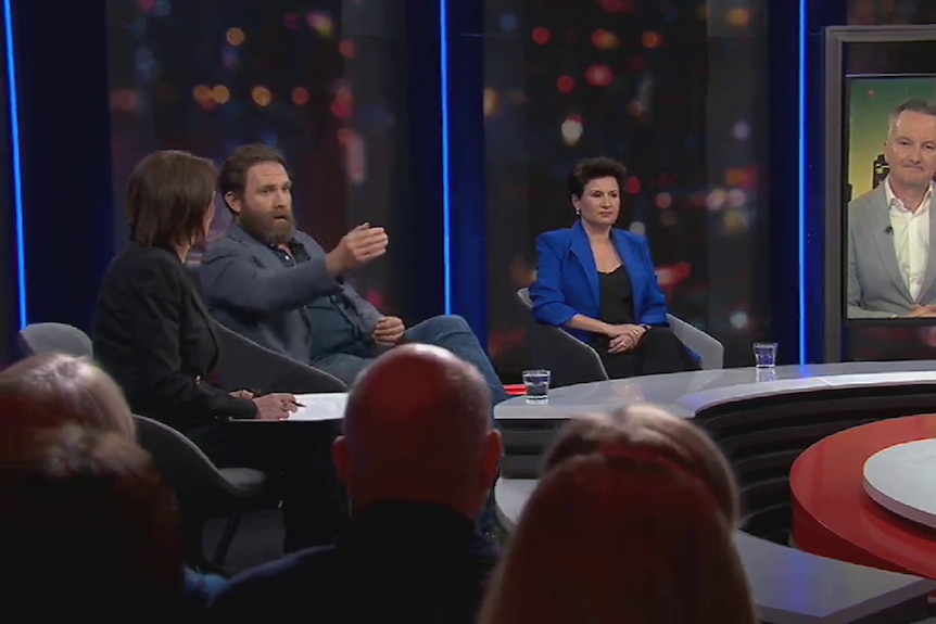 A wide shot of the Q+A panel showing Chris Bowen on a large video screen, and a bearded man talking.