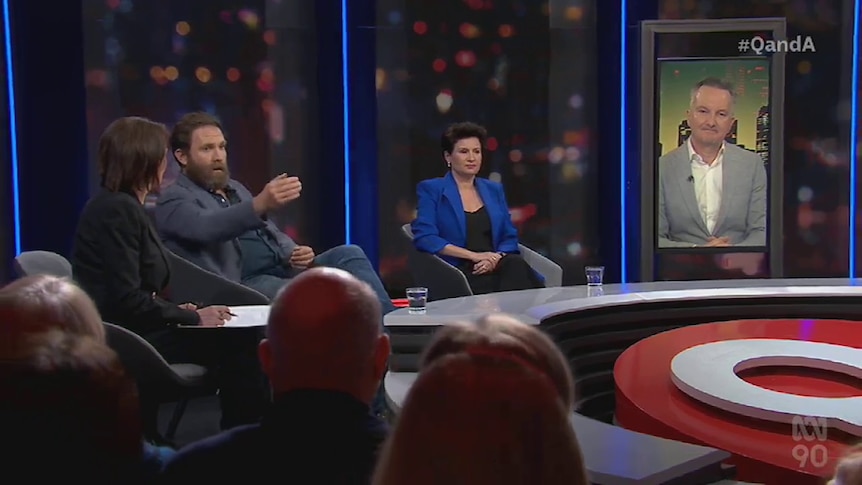 A wide shot of the Q+A panel showing Chris Bowen on a large video screen, and a bearded man talking.