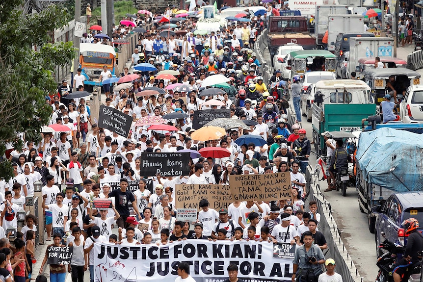 A crowd of mourners pack the streets and wave signs during a funeral march for Kian delos Santos.