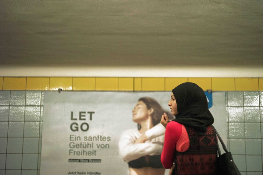 A woman in a hijjab stands in front of a German advertising board.