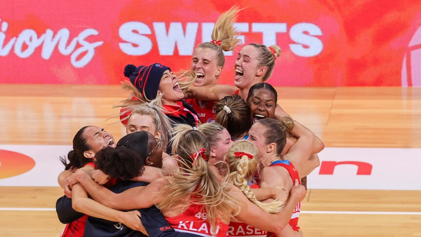 A group of Super Netball players jump around together in the middle of the court after winning a key final.