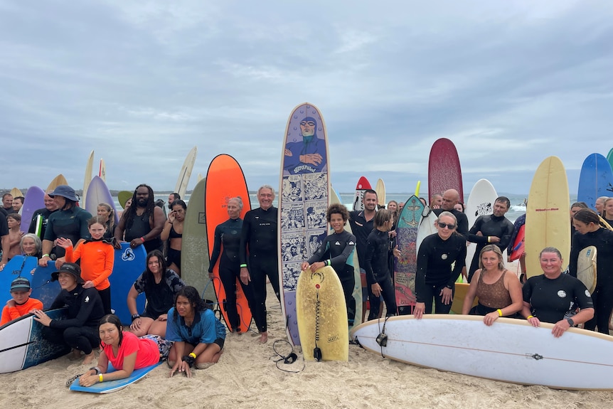 A group of surfers standing together on a beach, holding their boards.