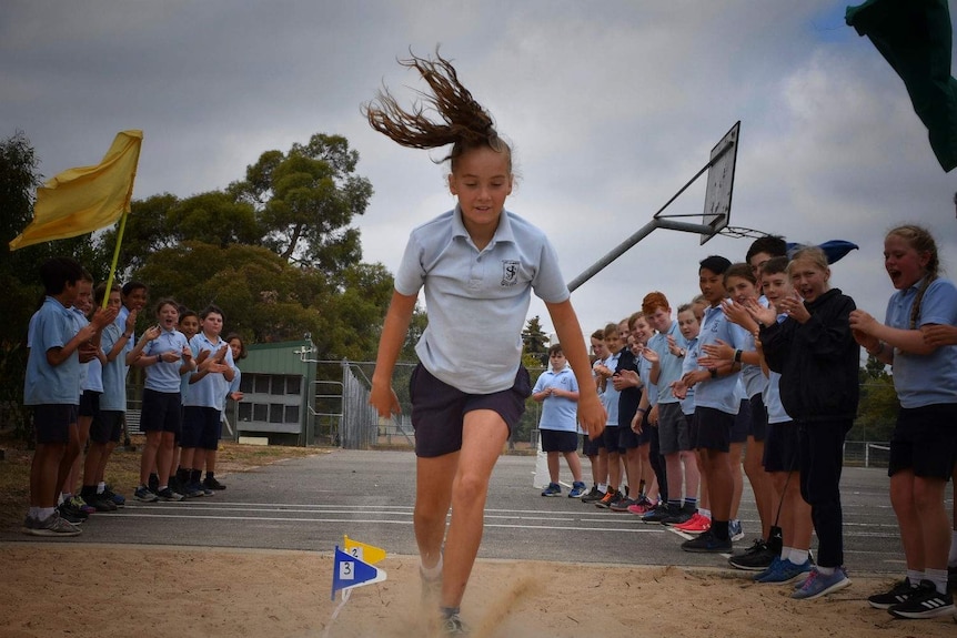 A child doing long jump into a sand pit.