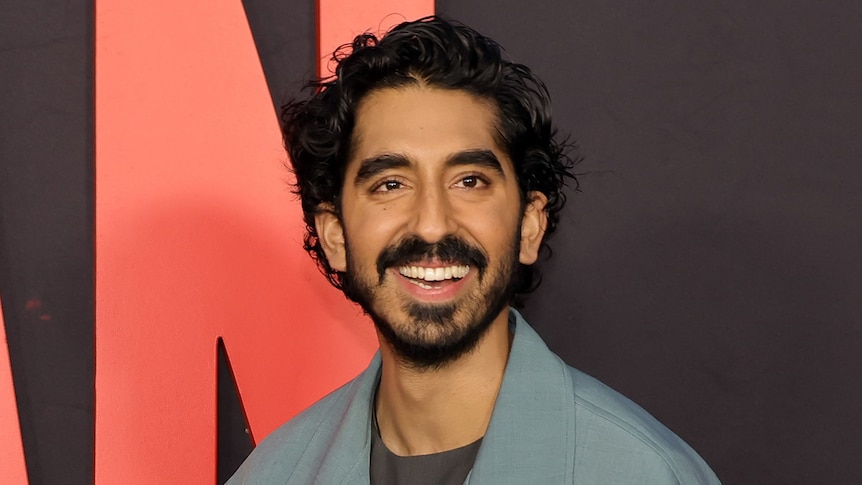A smiling black-haired man of South Asian descent wearing a grey suit on the red carpet