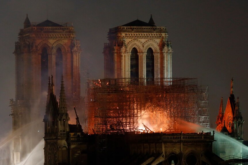 Firefighters spray water up to burning roof of a large cathedral