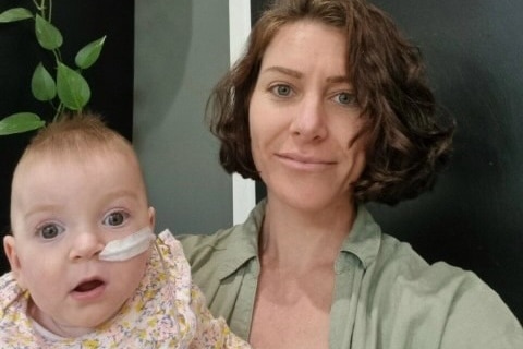 A baby with a tube coming from her nose, being held by a woman with dark wavy hair.