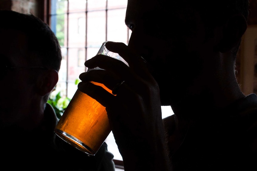 Silhouetted man drinks beer
