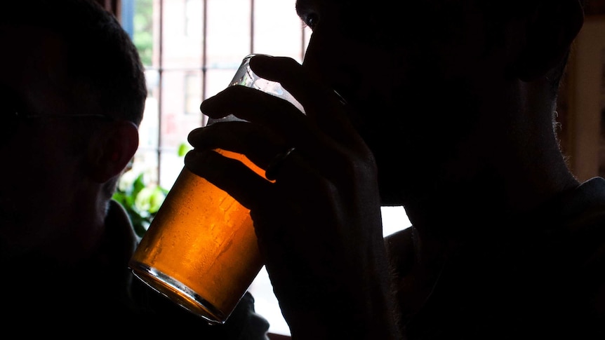 A silhouetted man drinks beer.