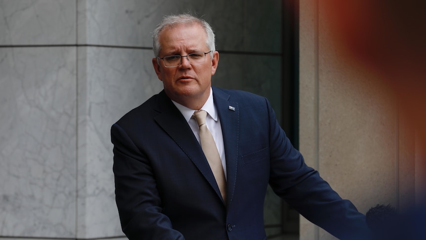 A man with grey hair and glasses wearing a suit and tie standing in a marble courtyard