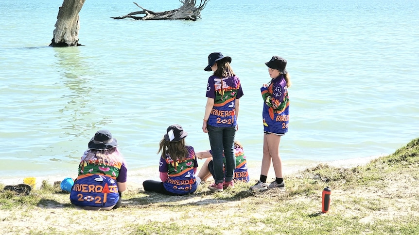 Six girls stand and sit near the Murray River wearing Girl Guides uniforms and hats.