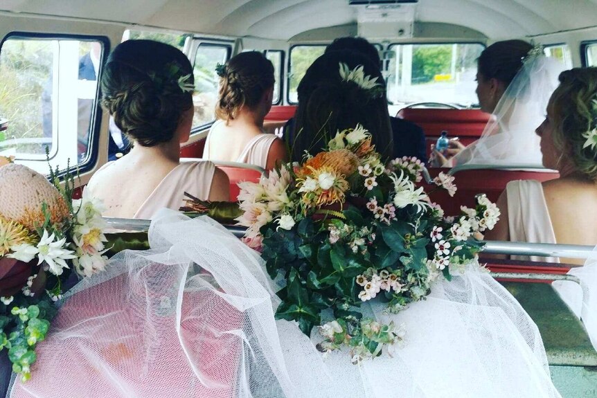 A bridal party sits inside the Kombi van, with bridal flowers in the foreground.