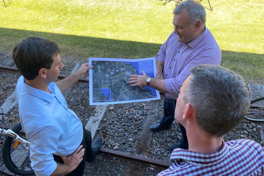 Bird's eye view of three men standing on a railway track examining a large paper satellite map.