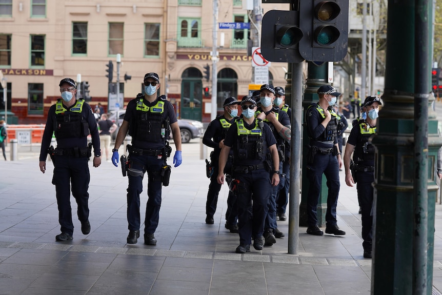 A group of police officers, all wearing masks, walk near Melbourne's Flinders Street Station.