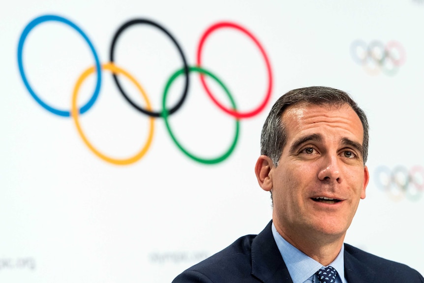 Eric Garcetti speaking with Olympic rings behind him.