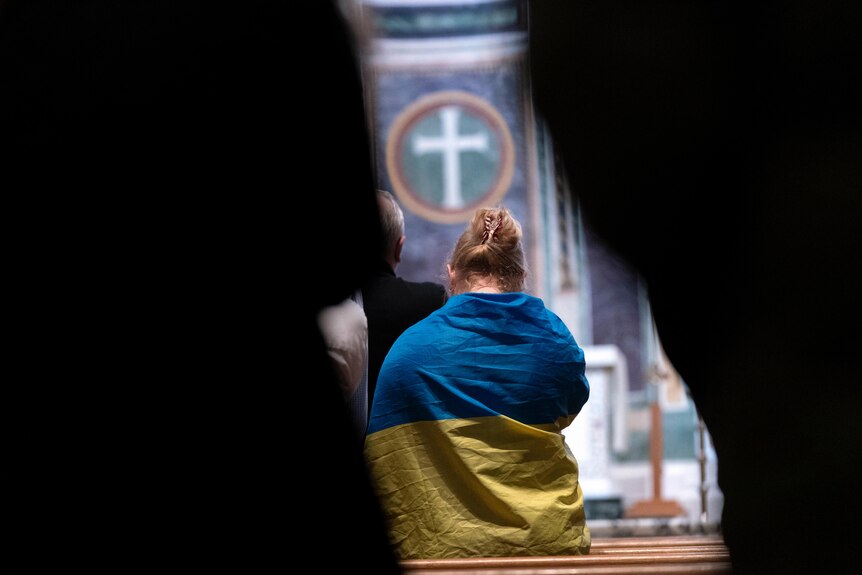 A woman in a Ukrainian blue and yellow flag with a cross suspended above her.