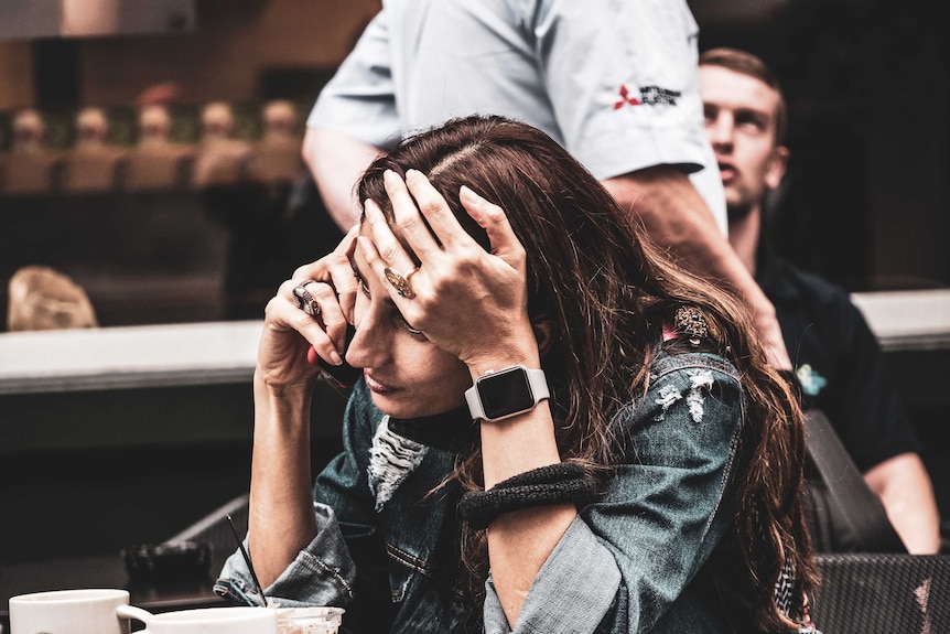 woman sitting at table, on the phone, looking worried