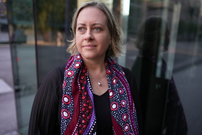 Alison Weatherstone wears dark top and colourful scarf. Looks off into the distance
