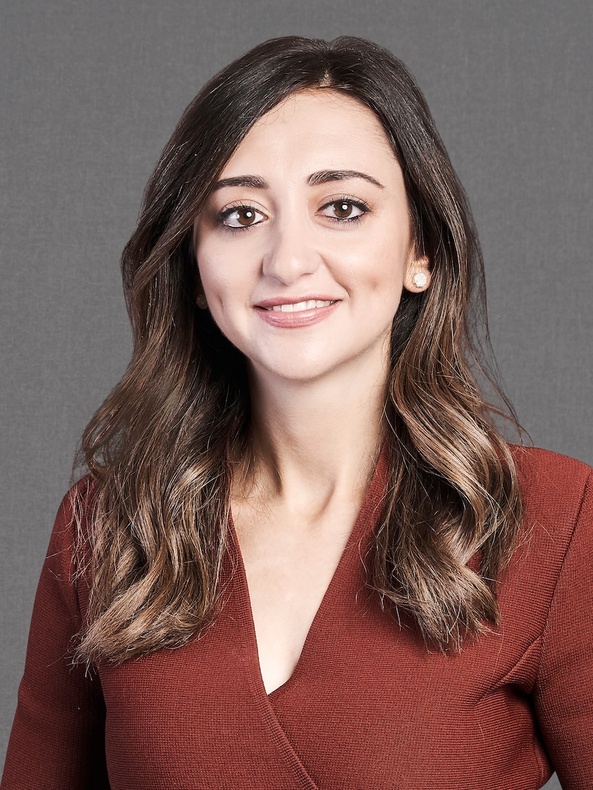 A portrait photo of a younger woman with brown hair with a maroon top on, smiling at the camera