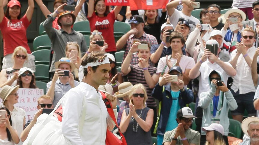Roger Federer walks out with his bag over his shoulder as fans celebrate behind him with banners.