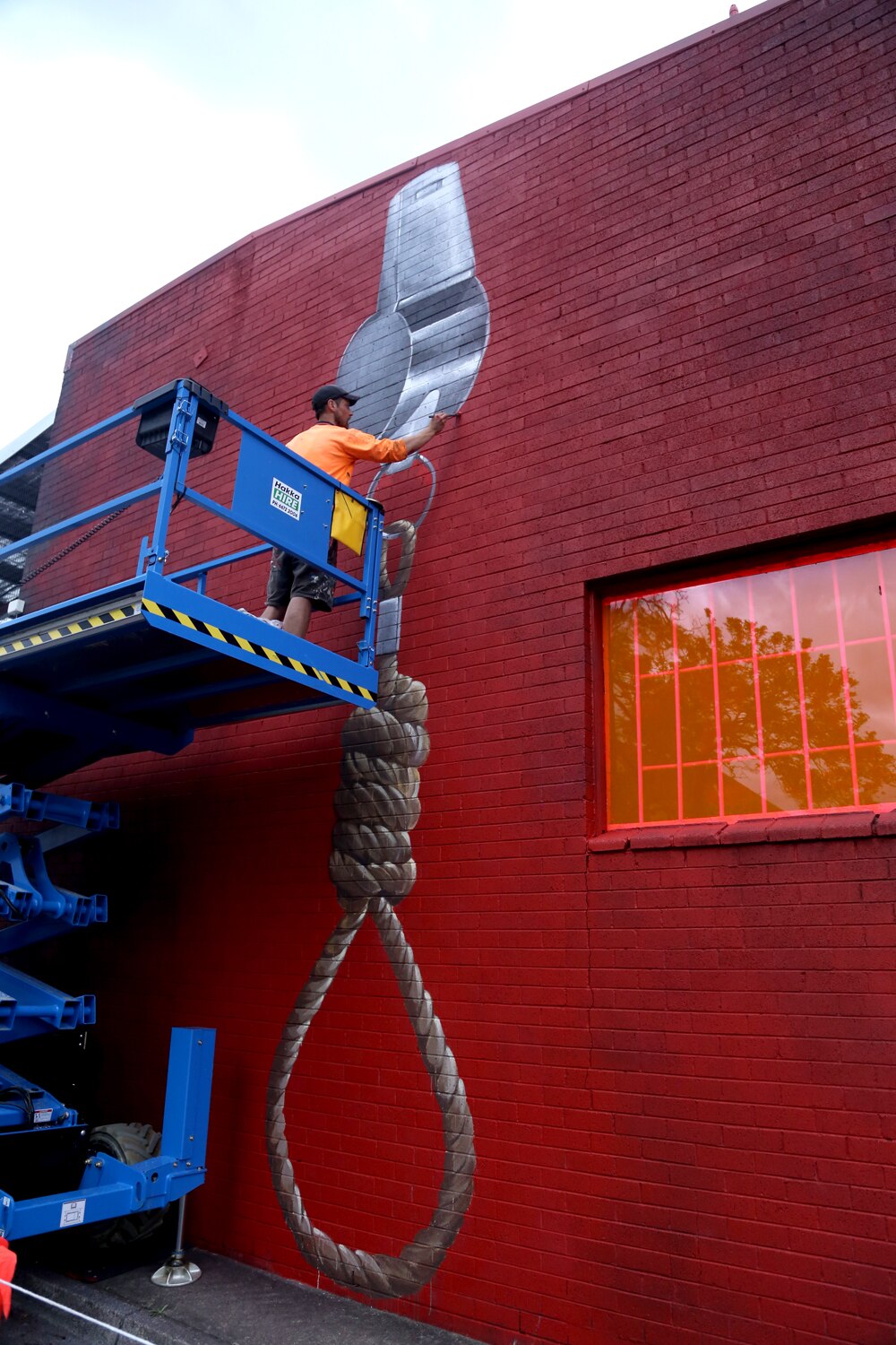 A mural on a red brick wall of a large silver whistle with a rope noose attached, hanging to the ground.