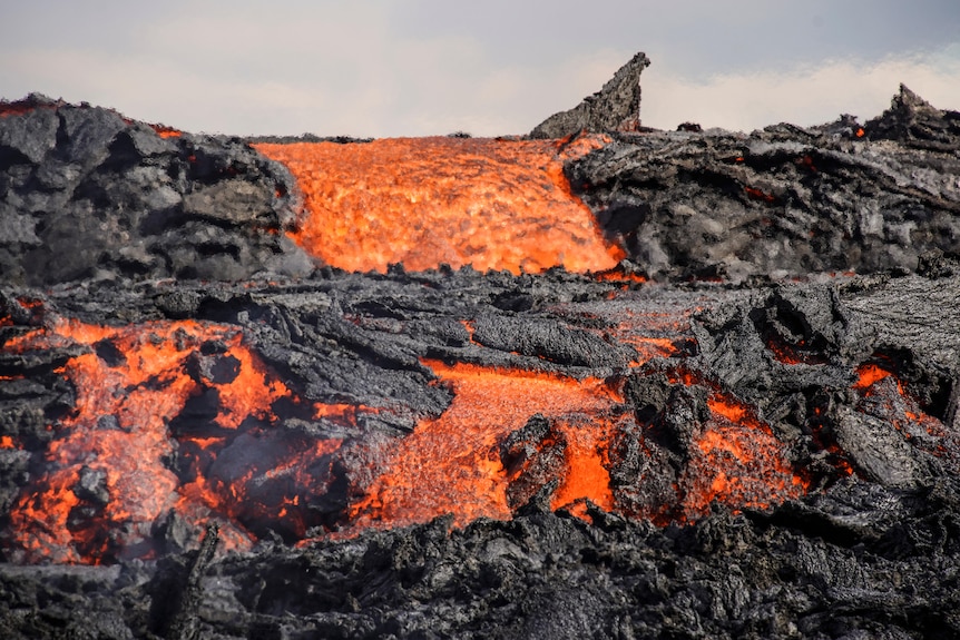 Multiple streams of glowing red lava flows down over black rock.