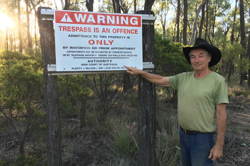 man pointing to a sign on a post in the bush.