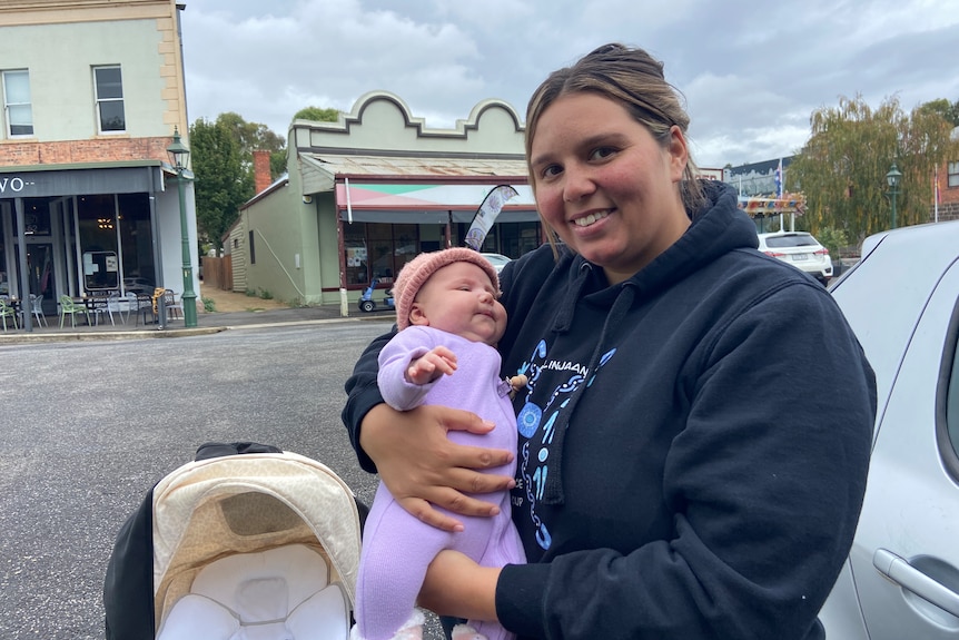 A woman wearing a blue hoodie holding a baby