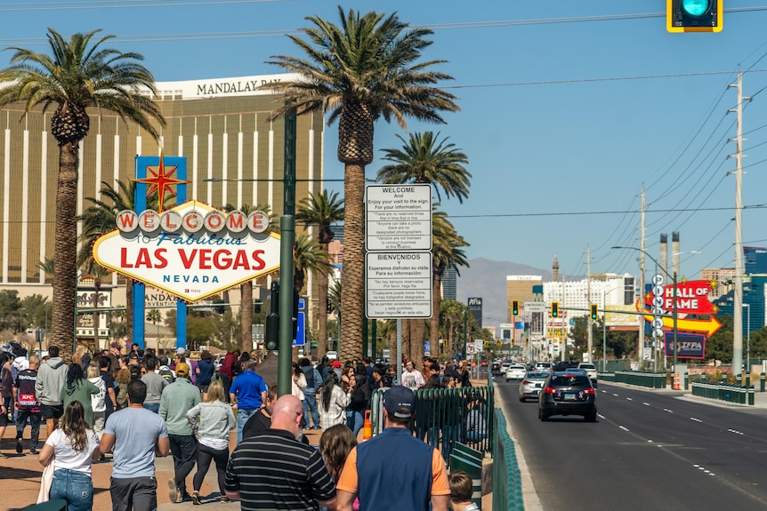 A bustling main street of Las Vegas full of people, palm trees and signs.