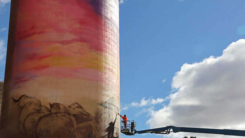 Artist on lift reaches high to paint a mural