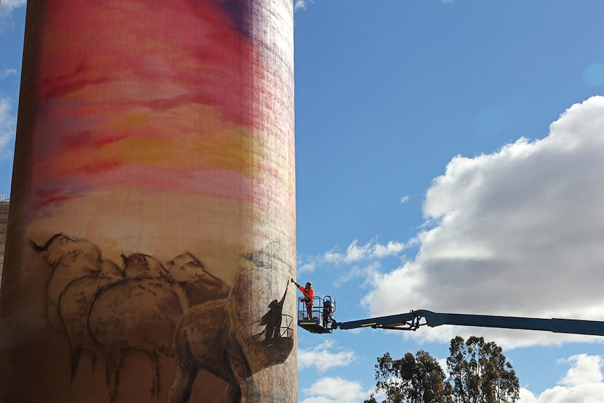 Artist on lift reaches high to paint a mural