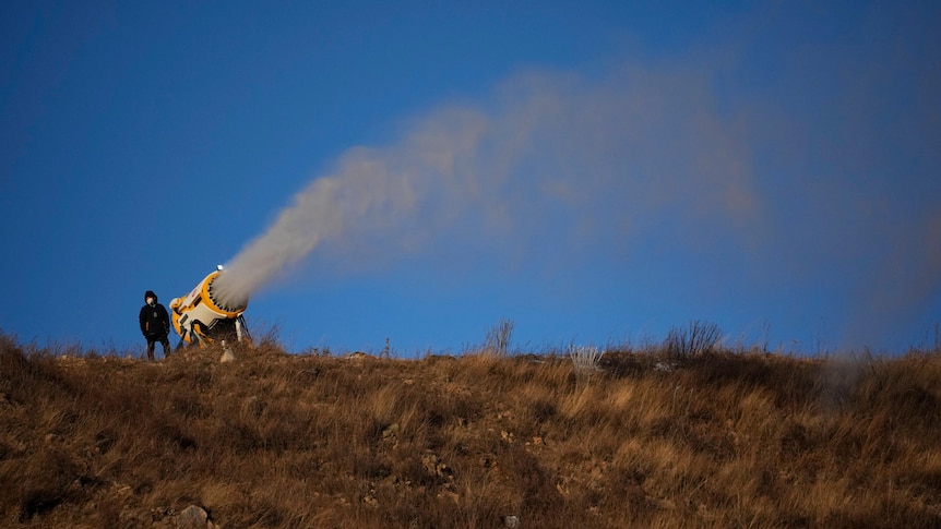 A person works at a snow making machine spreading snow on a hill.