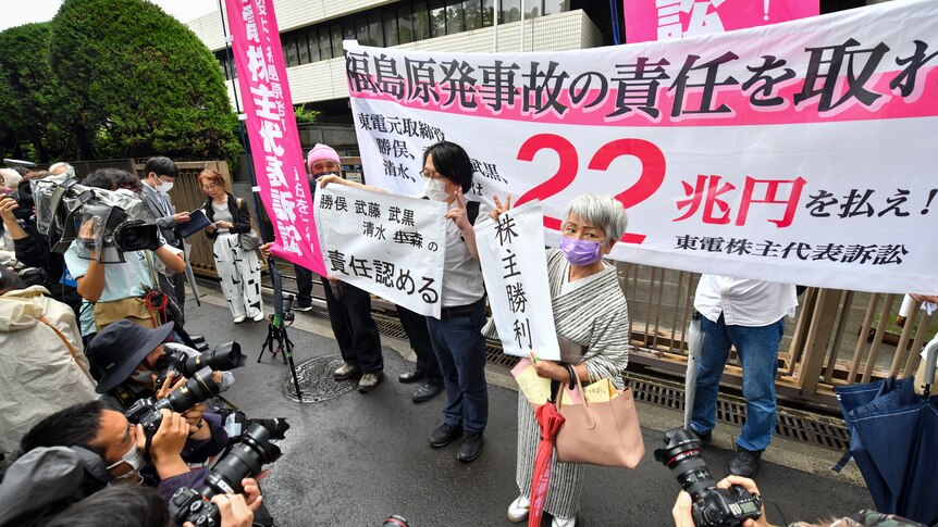 Journalists and photographers surround protesters holding banners and placards outside a courthouse in Japan