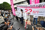 Journalists and photographers surround protesters holding banners and placards outside a courthouse in Japan