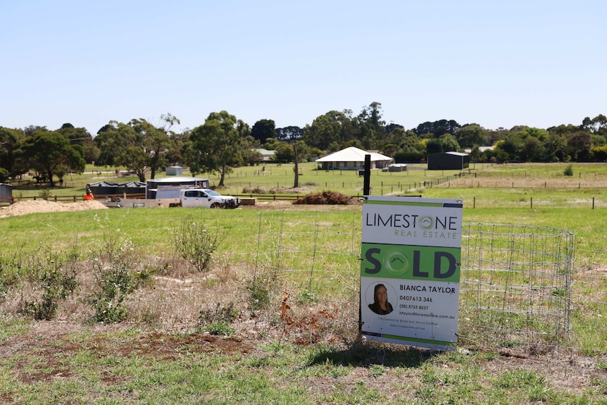 A sign reading "limestone real estate sold" sits in front of grass and construction workers