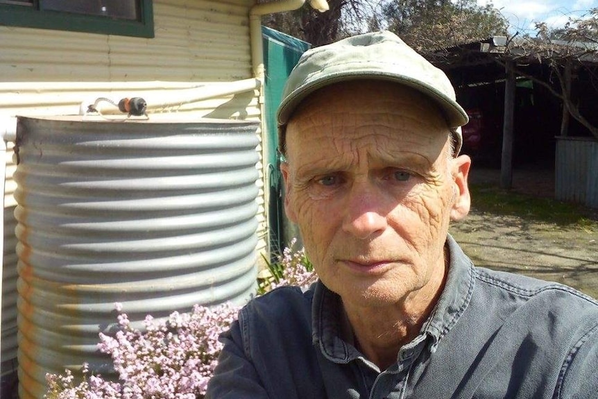 Elderly man takes photo of himself in front of water tank