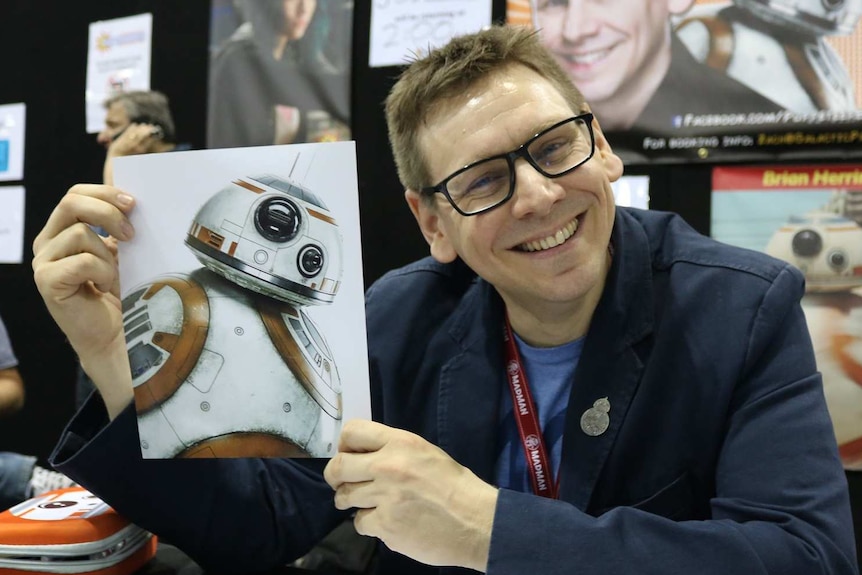 Brian Herring smiles holding up a picture of BB-8 at Supanova in Brisbane