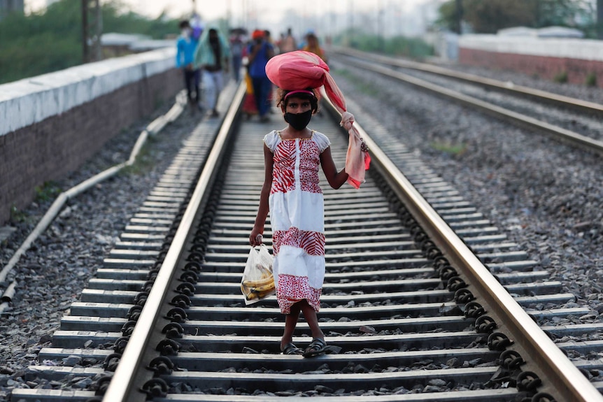 A girl wearing a long dress and a bag on her he walks along a railway track