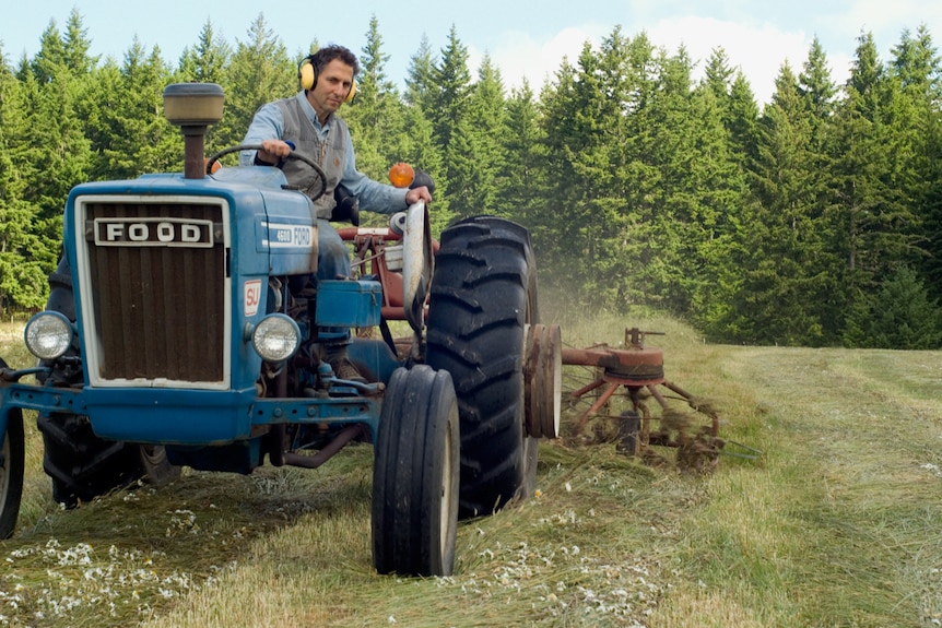 A man sits on a tractor in a wooded field.