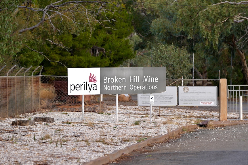 A sign at the Perilya mine in north Broken Hill in front of a fence and green trees.