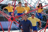 A man in a blue shirt poses for a photo with five primary school kids perched in a climbing apparatus